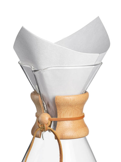 Clear glass coffee maker with wooden collar and white paper filter on a white background