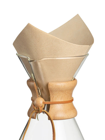Clear glass coffee maker with beige paper filter on a white background