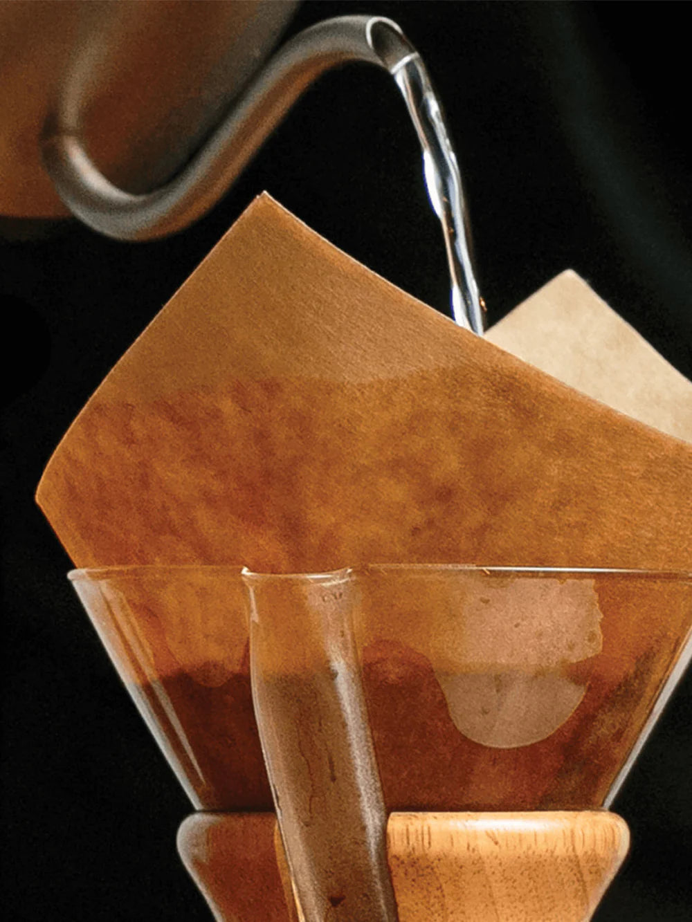 Coffee being poured into a glass with a paper filter on a dark background