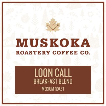 A square coffee label design for Muskoka Roastery Coffee Co. featuring a light cream background with faint winter tree illustrations, a gold maple leaf logo, and brown text reading 'MUSKOKA ROASTERY CO.